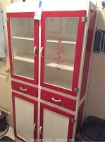 Front view of tall red and white wooden cabinet with glass doors, drawers and lower storage doors