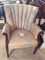 Front view of a pink and blue toned upholstered wooden armchair with scalloped padded back and curved wooden arms and legs.