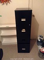 Front view of the black metal filing cabinet showing four drawer handles and lock.