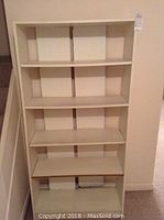 Large beige/tan bookcase with five shelves, signs of wear and bowing on shelves.