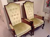 Two high-back upholstered armchairs with carved wood frames, cane sides and green velvet-like tufted upholstery.