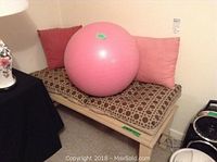 Bench with cushioned pad, showing wooden bench frame and pillows behind, includes pink exercise ball on seat