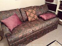 Front view of a floral pattern sofa bed with three seat cushions, three back cushions, two pink throw pillows, and one floral accent pillow. The fabric has a soft silky appearance.