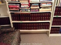 Shelves stocked with multiple volumes of National Geographic magazines in custom maroon sleeves with gold embossing, arranged on white shelving units, with some other books and furniture nearby.