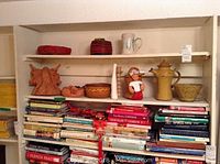 Two shelves with assorted artistic pottery pieces including vases, bowls, decorative sculptures, and figurines situated above a collection of books.