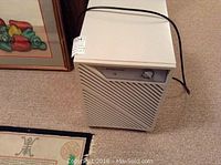 Full view of the beige Simplicity dehumidifier model 15 with ventilation panel and power cord, shown alongside a framed painting.