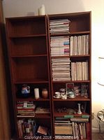 Two wooden shelving units filled with a mix of magazines and some glassware and teacup sets on the lower shelves.