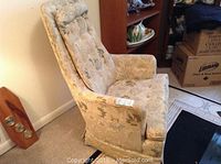 Side view of floral upholstered armchair showing button tufted high back and armrests, some visible wear on fabric.