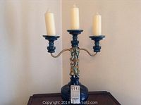 Front view of blue three-arm candelabra with three off-white taper candles, showing hanging decorative charms on the front column.