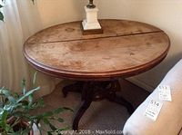 Photo of the top of the round wooden table showing wear, water stains and a seam in the middle, with a lamp on top.