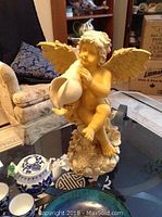 Closer image of resin angel statue holding conch shell, sitting on textured base.