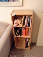 Front view of wood bookcase with books and a pig stuffed toy on shelves.