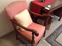 Front angle of the pink upholstered chair with wood scroll arms and white pillow, showing wear and condition of upholstery and wood.