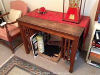 Solid wood desk table with a reddish tablecloth and decor on top, surrounded by furniture and stored items underneath.