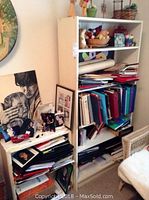 Smaller painted white wood bookcase filled with papers and framed photos, showing paint chips and wear.