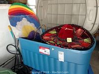 Blue plastic tote filled with various items including a red velvet sombrero and rainbow cloud kite.
