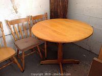 Wood round table with four matching chairs and two seat pads, showing wear and scuffs.