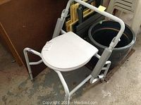 Photo of white metal commode chair with armrests and closed toilet seat lid.