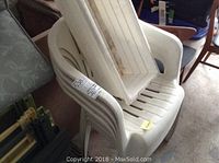 Four white resin stacking patio chairs with slatted design stacked together.