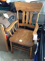 Wooden armchair showing carved backrest and curved armrests with a natural wood finish