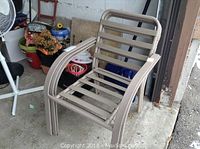 Photo of a stack of three brown metal and vinyl patio chairs with tubular frames, showing rust and brown vinyl seat and back slats.