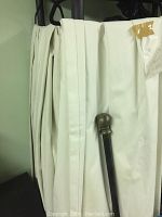 Folded drapes with attached curtain rod, showing pearl white fabric and rod finial