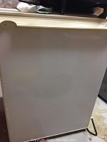 Side view of small white refrigerator showing chip on door handle and overall design.