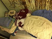 Photo of multiple handmade baby and toddler sweaters, some folded, including thick cable knit patterns and colorful patterned sweaters.