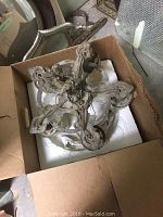 Top view of the chandelier inside an open box showing the five metal arms and central fixture base with wiring.