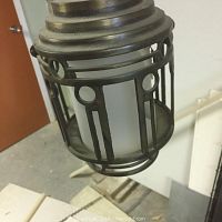 Close-up photo of the Art Deco style hanging lamp showing metal frame and part of the glass panel with a missing/broken piece.