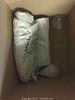 Box containing four chandelier bulbs wrapped in paper, one standard frosted bulb lying loose.