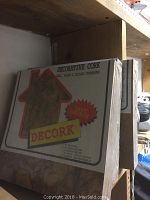 Three unopened packs of decorative cork tiles labeled DECORK on a shelf.