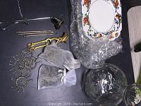 Overview of small items including brass napkin rings, nutcracker, nut picks, candle snuffer, dipping bowls, and decorative plates partially wrapped in bubble wrap.
