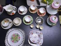 Full display of assorted fine bone china pieces including plates, saucers, cups, egg cups, coffee pot, water jug, and silver candy dish.
