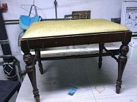 Side angled view of the wooden bench showing turned legs and vinyl seat.
