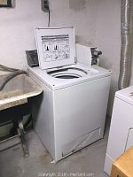 White Inglis commercial top-loading coin-operated washing machine with instruction label inside lid, showing wear and age.