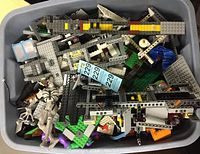 Overhead view into bin showing mixed gray Technic beams, green baseplates, various plates, slopes and two large figure torsos