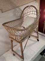 Rattan display crib showing woven open weave design with a cushion inside