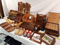 Overall lot showing multiple wooden household and decorative items arranged on a table covered with a white cloth, including trays, clogs, storage boxes, and framed artwork.