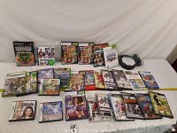 Photo showing a collection of video games on a white surface including titles for Xbox, PlayStation 2, PlayStation 3, and Nintendo DS platforms arranged in rows.
