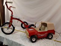Red metal tricycle and red beige Tonka metal toy jeep on white cloth background.