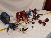 View of nine dragon figurines and a mythological figure on a white surface with measuring tape for scale.