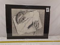 Full view of framed drawing showing two hands sketching each other, with black matting and glass frame.