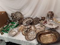 Full view of the silver plated items arranged on a table, featuring trays, cutlery, candlesticks and serving dishes.