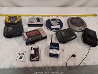 Overview of nine portable audio devices including various Walkman cassette players and CD players along with accessories such as batteries, an antenna, and a black carrying case.