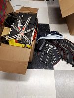 Box on floor filled with plastic railroad track pieces, switches, and electrical components