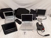 Photo shows multiple portable DVD players, camera bags, and accessories on a white background with lot number 53 sign.