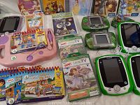 Close-up of LeapFrog LeapPad and Leapster devices with game cartridges and educational books around them.