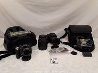 Wide view showing multiple digital cameras with lenses and two camera bags with accessories arranged on a table.