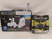 Wireless 60 gaming system box with 2 wireless controllers and Trivial Pursuit Digital Choice game box with handheld digital console visible, placed side by side.